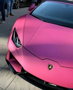 a pink lamb car parked on the side of a road next to other cars and people