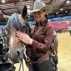 a woman in a cowboy hat petting a brown and black horse at an arena