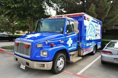 a blue emergency truck parked in a parking lot next to a silver car and trees