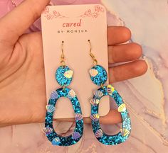 a pair of blue and gold colored earrings on a card with a hand holding it