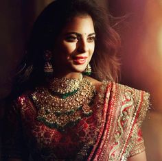 a woman in a red and gold outfit with jewelry on her neck, smiling at the camera