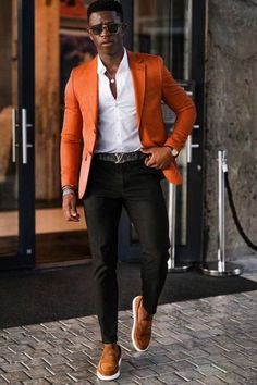 a man in an orange blazer and white shirt is walking down the street with his hands on his hips