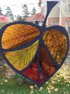 a heart shaped stained glass window hanging in front of a house with autumn leaves on it