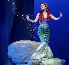 a woman dressed as the little mermaid standing on top of a rock