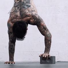 a man with tattoos doing a handstand in front of a white wall