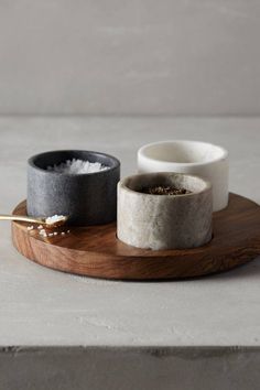 two bowls on a wooden tray with some salt and pepper in them next to each other