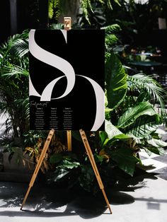 a black and white sign sitting on top of a wooden easel next to plants