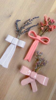 three pink and white hair clips on a wooden surface next to some dried flowers,