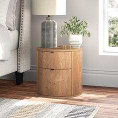 a nightstand with a plant on it next to a bed in a room that has hardwood floors and white walls