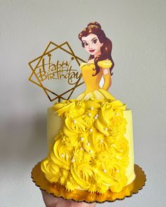 a hand holding up a yellow cake with frosting roses on it and a happy birthday card