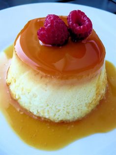 a dessert with two raspberries sitting on top of the cheesecake covered in caramel sauce