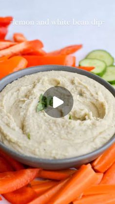 a bowl filled with dip surrounded by carrots and cucumbers