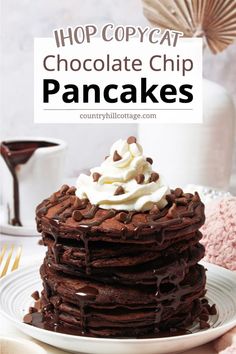 a stack of chocolate pancakes topped with whipped cream and chocolate chips, on a white plate