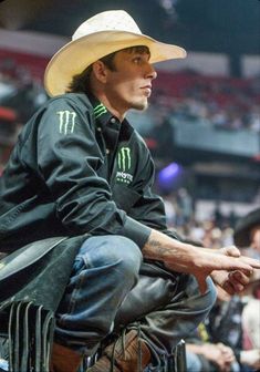 a man wearing a cowboy hat sitting on top of a chair in front of a crowd