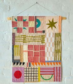 a wall hanging on the side of a white brick wall with an abstract quilt design