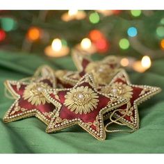 three red and gold star ornaments sitting on a green cloth with lights in the background