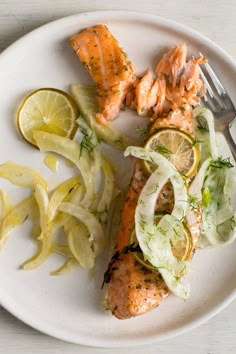 a white plate topped with salmon, onions and lemon wedges next to a fork