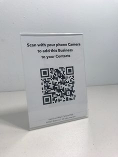 a white sign with a qr code on it that says scan with your phone camera to add this business to your contacts