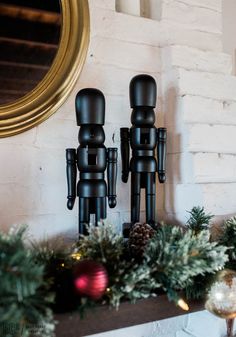 two wooden toy figures sitting on top of a mantel covered in christmas greenery