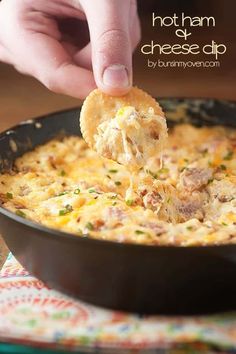 a person dipping cheese into a skillet filled with macaroni and cheese dip