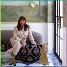 a woman sitting on top of a couch in front of a wall with a painting