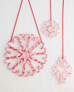 two red and white ornaments are hanging from strings on a wooden surface, one is shaped like a snowflake