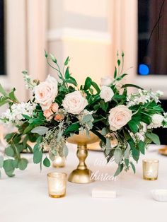 flowers and greenery are arranged in gold vases on a white tablecloth with candles