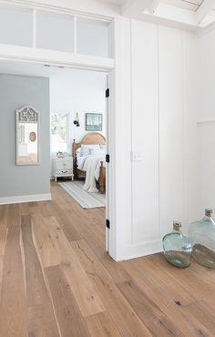 an open door leading to a bedroom with white walls and wood floors, along with two vases on the floor