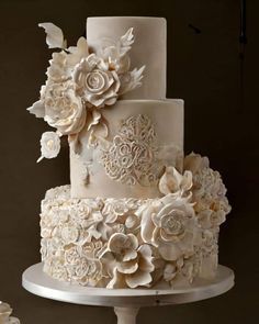 a three tiered wedding cake with white flowers on the top and bottom, sitting on a pedestal