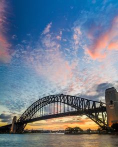 the sydney harbour bridge at sunset as seen from across the water with clouds in the sky