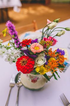 a vase filled with colorful flowers sitting on top of a white tablecloth covered table