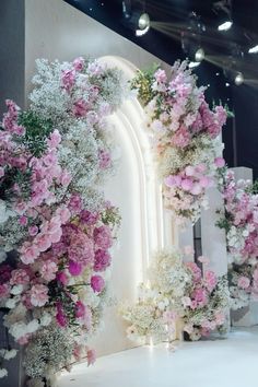 flowers and greenery are arranged in front of a large mirror at the entrance to a building