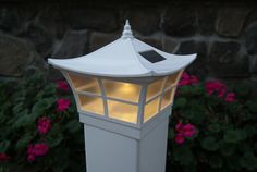 a small white light that is on top of a lamp post in front of some flowers