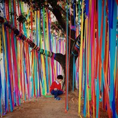 a person sitting on the ground in front of a tree with streamers hanging from it