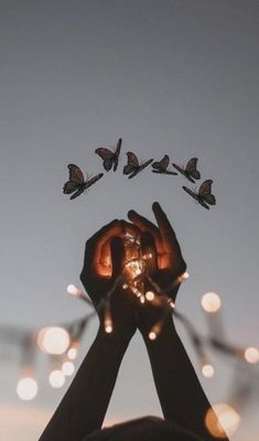 a person holding their hands up to the sky with some butterflies flying above them in the air