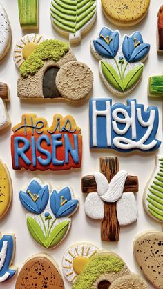 decorated cookies with the words he is risen displayed on a white table top, surrounded by blue and green decorations