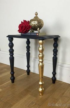 a black and gold end table with a red rose on top, next to a white wall