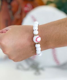 a person wearing a white beaded bracelet with red and white baseballs on it