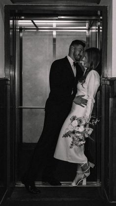 black and white photograph of a couple kissing in an elevator with their arms around each other