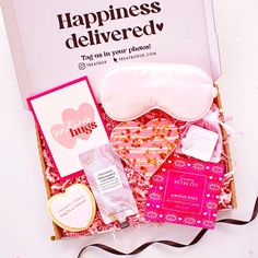 an open box with pink and white items in it, including eye mask, heart shaped candies, valentine's day cards, and more