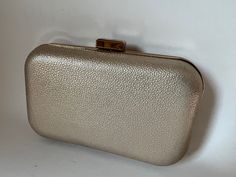 "This Jessica Simpson brand case is covered in light gold-color textured vinyl over the hard shell and is roomy enough for your evening essentials. The bag has a bright gold-color frame, rectangular tip-up clasp, and hinges. The interior is lined in champagne or ivory fabric. Including the clasp, the bag is 4 1/4\" high x 6 1/2\" wide x 1 7/8\" thick. To open, tip up the lower edge of the clasp. One slight blemish on back (pictured)." Classic Gold Clutch With Gold-tone Hardware, Elegant Metallic Rectangular Evening Bag, Classic Gold Clutch For Events, Metallic Rectangular Clutch For Formal Events, Metallic Rectangular Clutch For Formal Occasions, Gold Rectangular Case Clutch For Formal Occasions, Classic Gold Clutch For Party, Gold Rectangular Clutch For Formal Occasions, Gold Rectangular Clutch