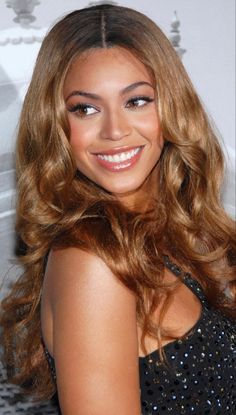 a woman with long, wavy hair smiles at the camera while wearing a black dress