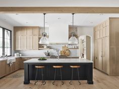 a large kitchen with wooden cabinets and stools in it's center island surrounded by wood flooring