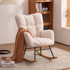 a rocking chair with a blanket on it in front of a book shelf and window