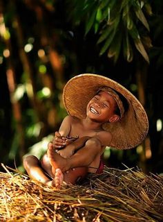 a young boy in a straw hat sitting on the ground with his arms around him