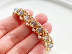 a hand is holding a gold and white beaded bracelet with pearls on the end