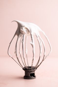 a whisk with white icing on top of it in front of a pink background