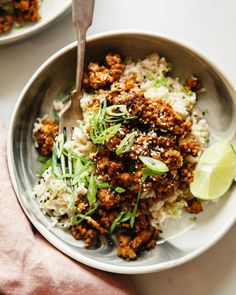 a bowl filled with rice and meat on top of a white table next to a pink napkin