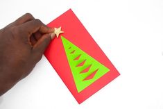 someone is cutting out a christmas card with a star on the top and green trees on the bottom