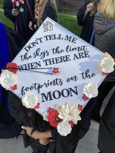 Grad cap that reads "Don't tell me the sky's the limit when there are footprints on the moon." It's white with flowers and rhinestones around the edges. White Grad Cap Decoration, Artsy Grad Cap Ideas, Graduation Cap Designs Meaningful, Baseball Graduation Cap Ideas, Grad Cap Inspo Sza, Space Themed Graduation Cap, Almost There Graduation Cap, Cute Graduation Caps High Schools